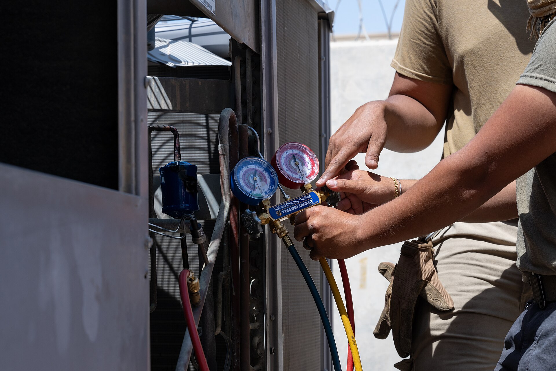 Technicians checking refrigerant gauges on an outdoor AC unit